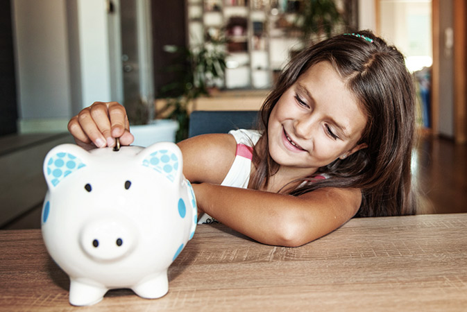 Child putting money in piggy bank.
